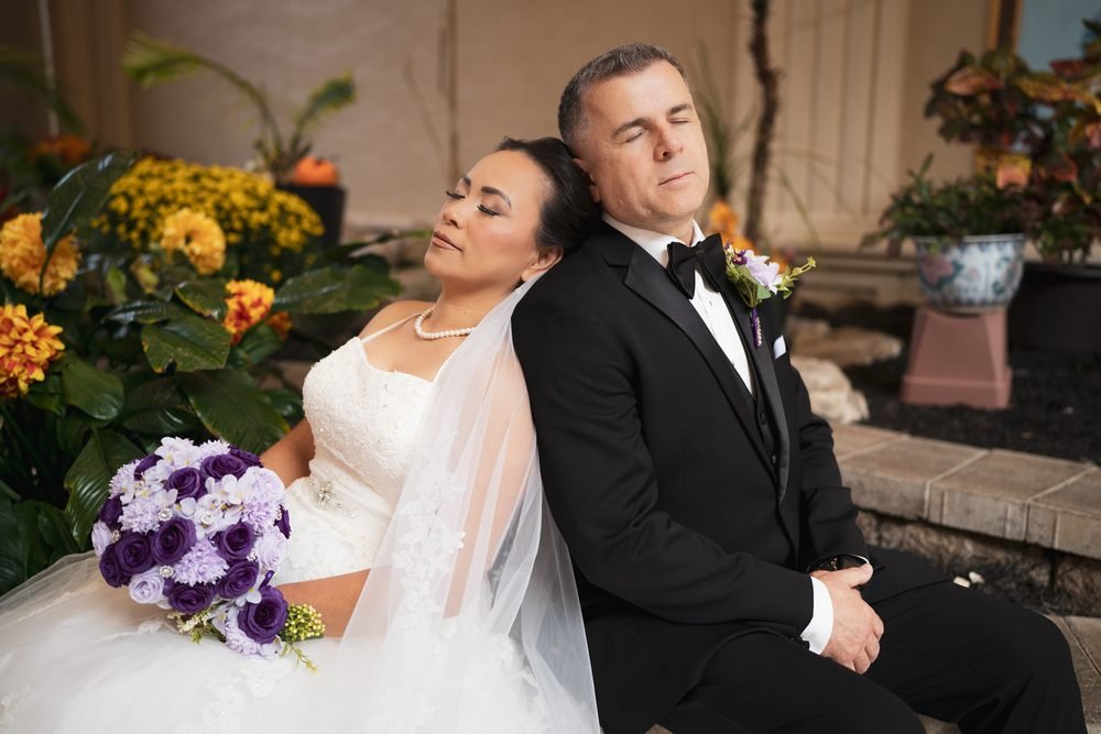 Bride and groom resting back to back among the atrium flowers at the Giovanni Caboto Club