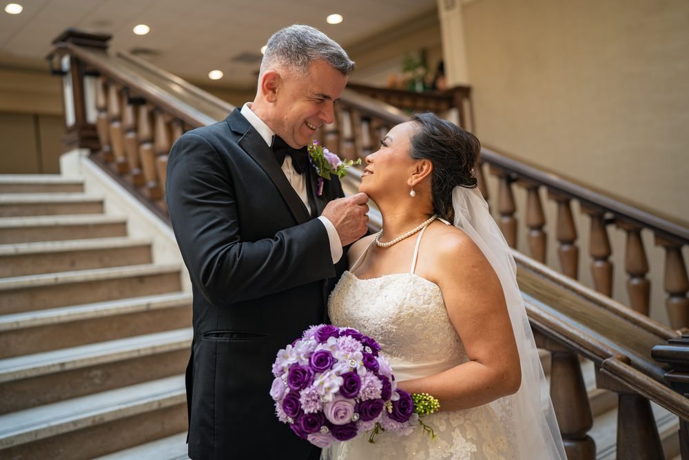 Groom lifting his bride's chin as they laugh on the Caboto Club staircase in Windsor